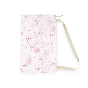 May include: White drawstring bag with a pink floral pattern and pink bows. The bag has a personalized monogram "CMP" in the center.