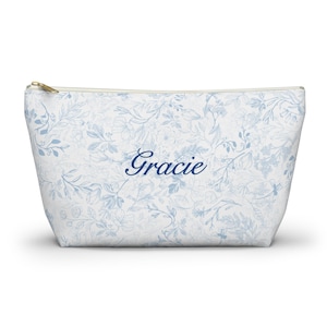 May include: A white zippered pouch with a blue floral pattern and the name "Gracie" embroidered in blue.