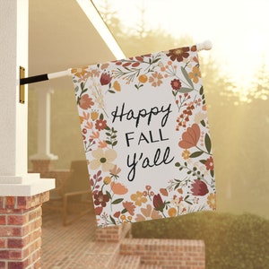 May include: A rectangular outdoor flag with the text "Happy Fall y'all" in black script. The flag is decorated with a floral wreath in shades of orange, brown, and cream. The flag is mounted on a white pole.