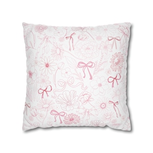 May include: A white pillow with a pink floral pattern and pink bows. The pillow is made of soft fabric and has a comfortable feel.