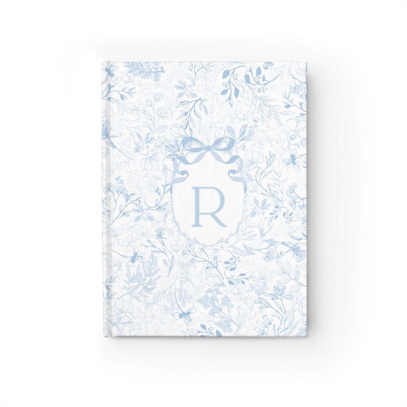 May include: A blue and white floral patterned journal with a white monogrammed initial "R" in a blue ribbon bow.