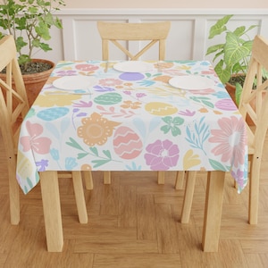 May include: A white tablecloth with a pastel floral and egg pattern. The tablecloth is laid on a wooden table with four wooden chairs.