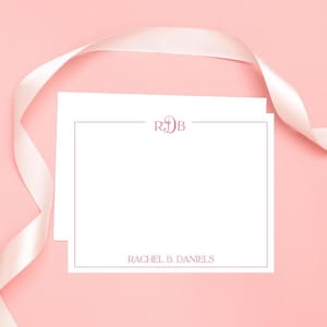 以下が含まれることがあります： ピンク色の縁取りと上部に「RDB」のイニシャルが入った2枚の白いノートカード。下部には「RACHEL B. DANIELS」という名前が印刷されています。ピンク色の背景にピンク色のリボンがかけられています。