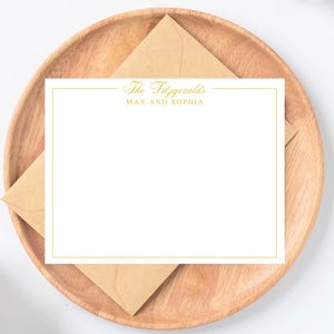 May include: A white stationery card with a gold border and the text "The Fitzgeralds MAX AND SOPHIA" is displayed on a wooden plate with a brown envelope. The stationery is blank, ready for personalization.