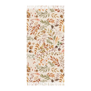 May include: A beige table runner with a pattern of brown, orange, and green leaves and berries. The runner has a white fringe on both ends.