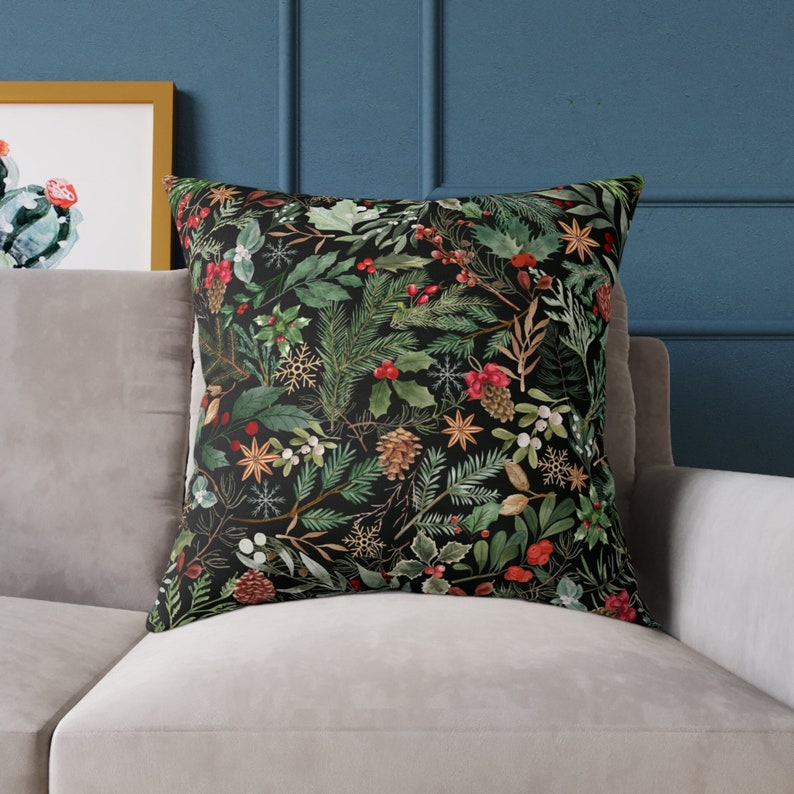May include: A black throw pillow with a festive holiday design featuring green pine branches, red berries, and white snowflakes.