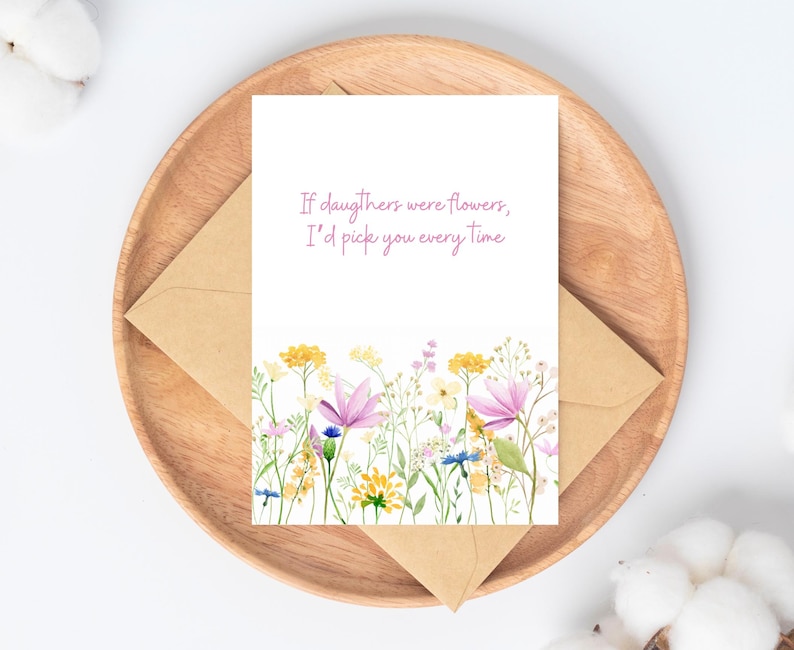 Peut inclure: Une carte de v&oelig;ux avec un motif floral et le texte "If daughters were flowers, I'd pick you every time." La carte est sur un plateau en bois avec une enveloppe en papier kraft.