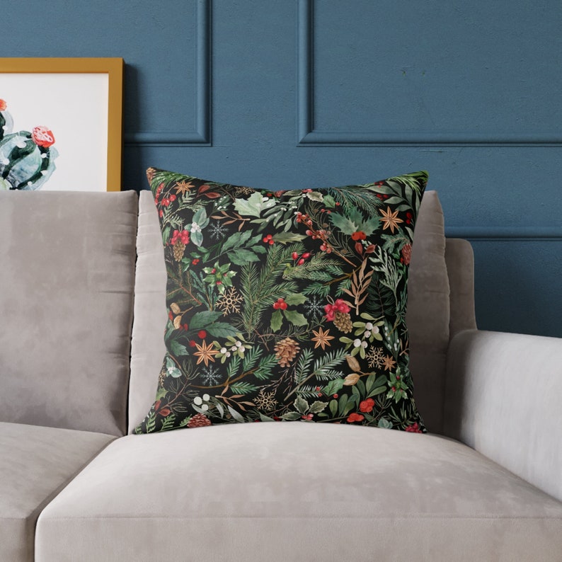 May include: A black throw pillow with a festive holiday pattern featuring green pine branches, red berries, and gold accents.
