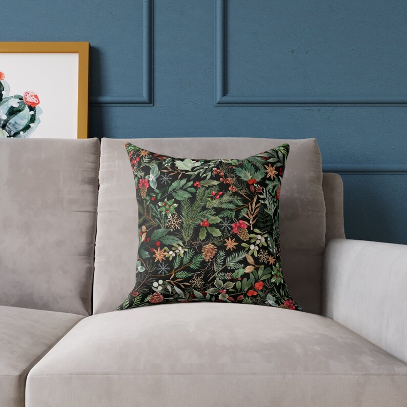 May include: A black throw pillow with a festive holiday pattern featuring green pine branches, red berries, and gold accents on a black background.