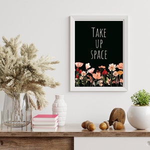 May include: A black and white printable wall art print with the text "TAKE UP SPACE" in white lettering. The print features a floral border of pink, orange, and red flowers on a black background.