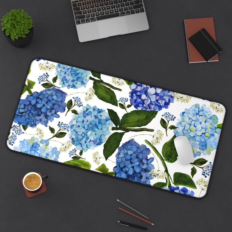May include: A white desk mat with a blue and green floral pattern. The pattern features watercolor-style hydrangeas and leaves.