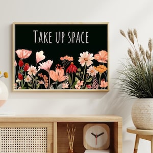May include: A framed print with a black background and a floral design. The text "TAKE UP SPACE" is written in white letters on the print.
