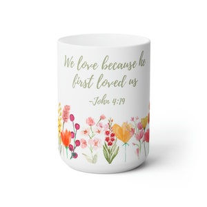 May include: White ceramic mug with a floral design and the quote "We love because he first loved us - John 4:19".
