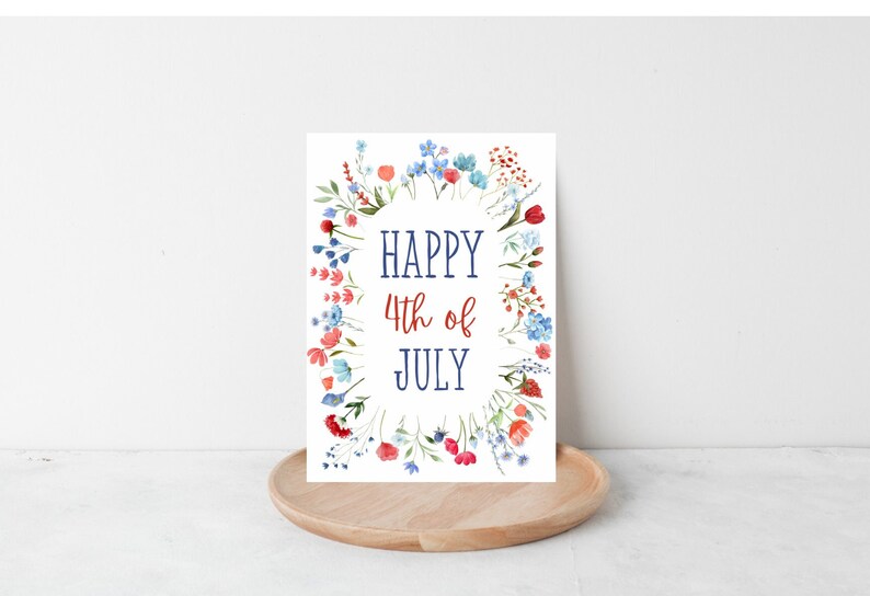 May include: A white card with a wreath of red, blue, and pink flowers surrounding the text "HAPPY 4th of JULY" in blue and red lettering.