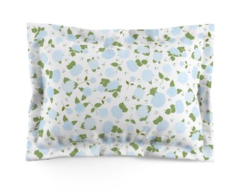 May include: A rectangular pillowcase with a white background, covered in a pattern of light blue hydrangea flowers and green leaves. The pillowcase has a ruffled edge and is designed for a standard pillow.