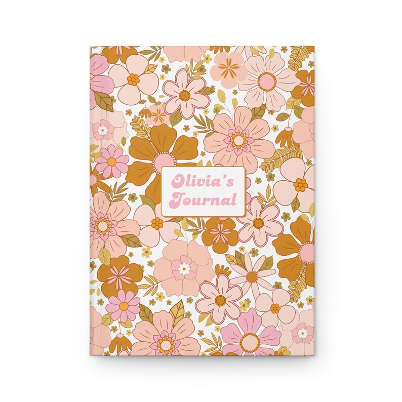 May include: A personalized journal features a retro floral design in shades of pink and gold on a white background. The cover displays the name 'Olivia's Journal' in a pink, retro-style font within a rectangular box. The overall aesthetic is reminiscent of 1970s patterns. The journal is a perfect gift for journaling enthusiasts and those who appreciate vintage designs.
