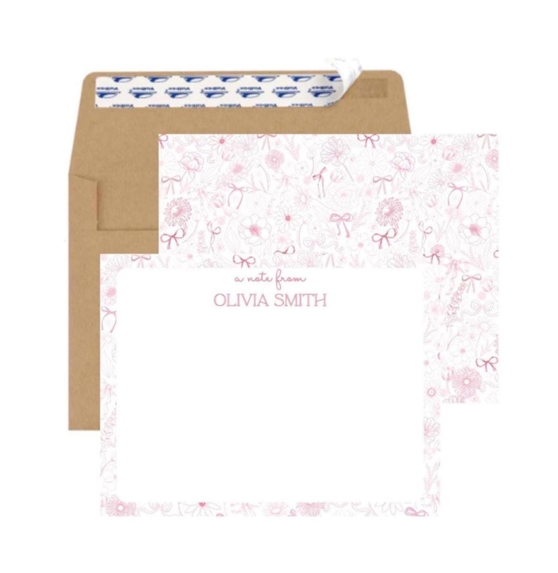 May include: A white note card with a pink floral border. The card has the text 'a note from' and 'OLIVIA SMITH' printed in pink. The card is displayed with a brown envelope.