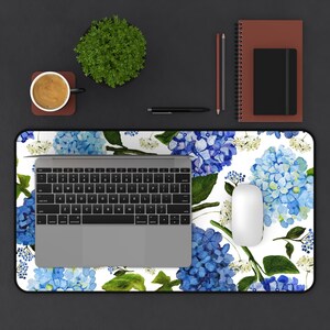May include: A white desk mat with a blue and green floral pattern. The mat features a watercolor design of hydrangeas and leaves. A laptop, mouse, and other office supplies are on the desk.