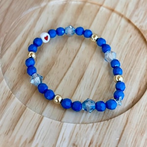 May include: A blue beaded bracelet with gold accents and a white heart charm with a red center.