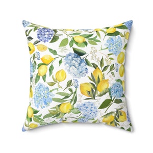 May include: A white throw pillow with a watercolor pattern of lemons, blue hydrangeas, and green leaves.