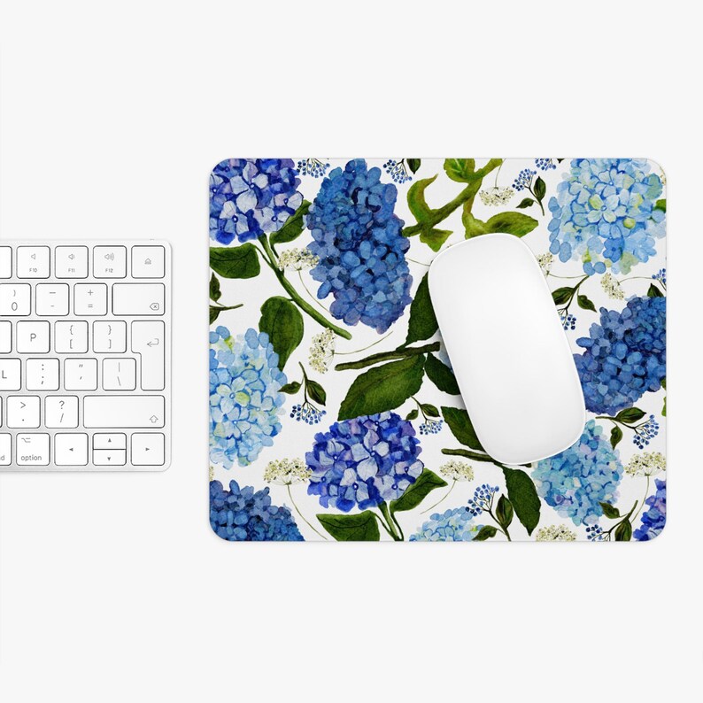 K&ouml;nnte beinhalten: Eine wei&szlig;e Mausmatte mit einem blauen und gr&uuml;nen Blumenmuster mit Hortensien. Die Mausmatte ist f&uuml;r die Verwendung mit einer Computermaus konzipiert.