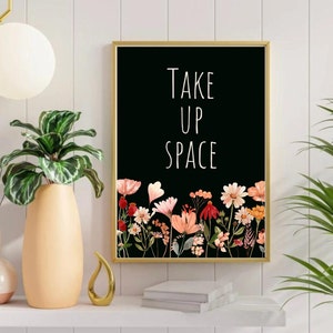May include: Black and white print with the text "Take Up Space" in white lettering. The print is framed in gold and features a border of pink, red, and orange flowers.