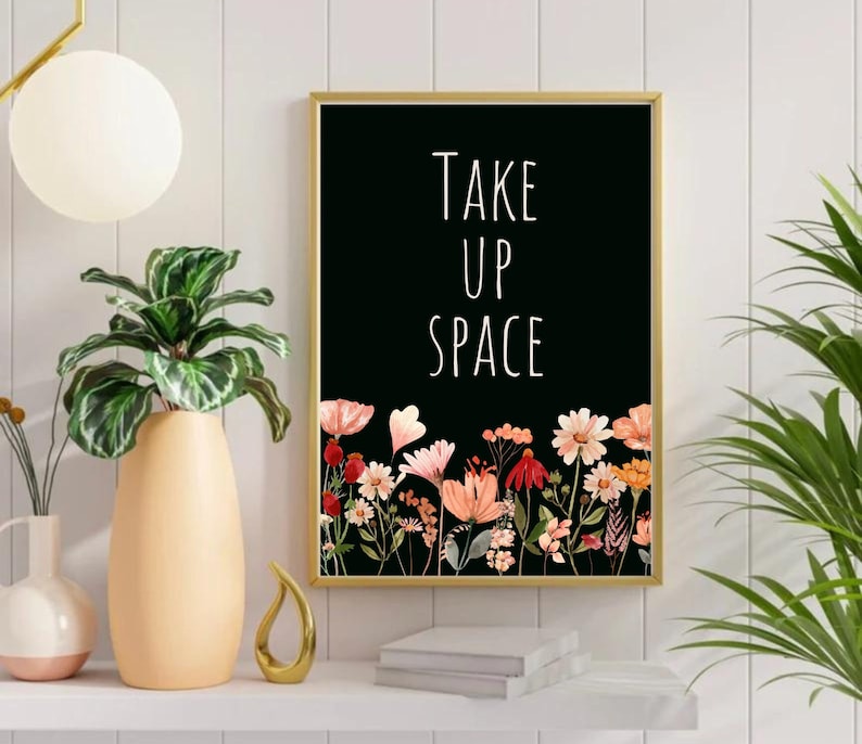May include: Black and white print with the text "Take Up Space" in white lettering. The print is framed in gold and features a border of pink, red, and orange flowers.