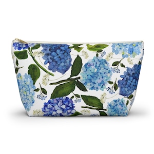 Puede incluir: Una bolsa blanca con cremallera con un estampado floral con hortensias azules y moradas sobre un fondo blanco.