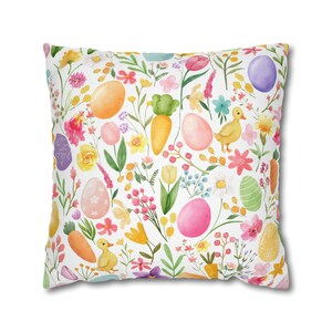 May include: A white cushion with a colourful Easter pattern. The pattern features pastel coloured eggs, carrots, flowers, and ducklings.
