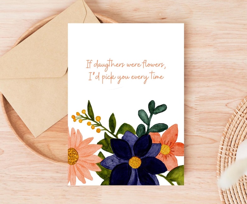 Peut inclure: Carte de v&oelig;ux blanche avec le texte "Si les filles &eacute;taient des fleurs, je te choisirais &agrave; chaque fois" et des illustrations florales roses, oranges et bleues. Une enveloppe en papier kraft est pos&eacute;e sur un plateau en bois.