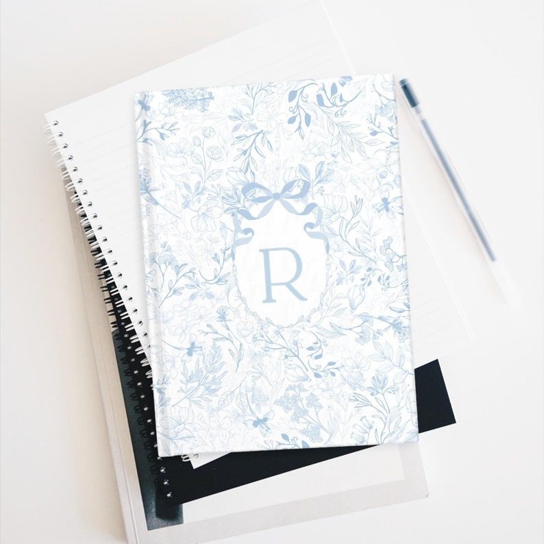 May include: A blue and white notebook with a floral pattern and a monogrammed letter "R" in a decorative frame.
