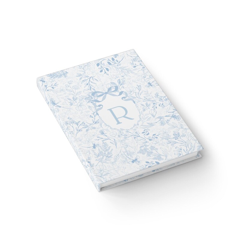 May include: A blue and white floral patterned journal with a monogrammed initial "R" in a crest.