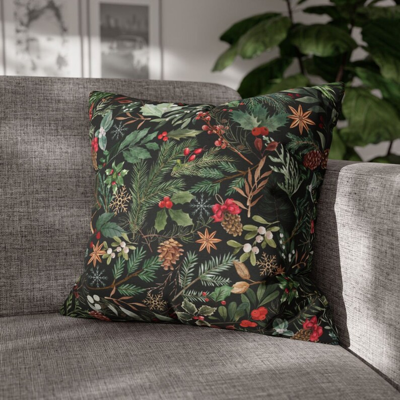 May include: A black throw pillow with a festive holiday pattern featuring green pine branches, red berries, and white snowflakes.