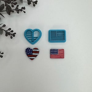 May include: Four cookie cutters: two are blue and shaped like the American flag, one is blue and shaped like a heart, and one is red, white, and blue and shaped like a heart.