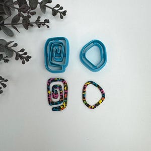 May include: Four cookie cutters, two are blue and two are colorful. The blue cutters are a spiral and a rounded shape. The colorful cutters are a spiral and a rounded shape.