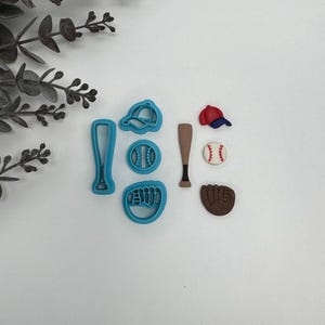 May include: A collection of baseball-themed items, including a baseball bat, glove, ball, and cap. The set includes blue plastic cookie cutters and a baseball with red stitching. A brown baseball bat and glove are also present.