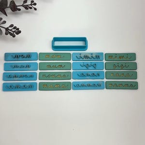May include: A set of 18 blue and green polymer clay stamps with gold lettering. The stamps feature various names, including Mimi, Gigi, and Nana. A blue plastic rectangle stamp is also included.