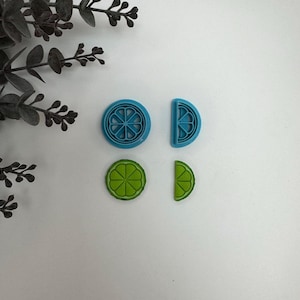 May include: Four blue and green plastic cookie cutters shaped like limes. Two cutters are whole limes and two are lime wedges.