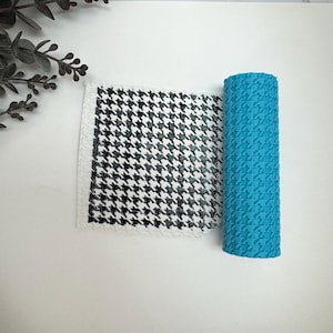 May include: A roll of blue patterned material next to a piece of fabric with a black and white houndstooth design. The fabric is white with a black pattern. The blue roll has a repeating pattern.