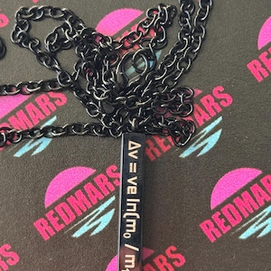 May include: A black chain necklace with a rectangular pendant. The pendant has a formula printed on it in white. The background is black with a repeating pattern of pink and blue text that says "REDMARS".