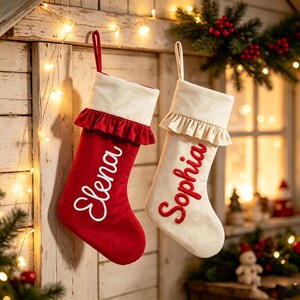 Könnte beinhalten: Zwei Weihnachtsstrümpfe mit Aufhängeschlaufen. Einer ist rot mit weißem, in Schreibschrift gesticktem Namen Elena und weißem Rüschenbündchen. Der andere ist weiß mit rotem, in Schreibschrift gesticktem Namen Sophia und weißem Rüschenbündchen.