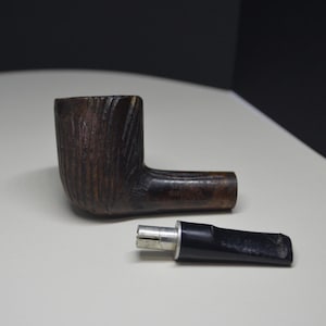 May include: A disassembled tobacco pipe. The bowl is dark brown and textured, while the stem is black. The pipe is made of wood and is lying on a light surface.