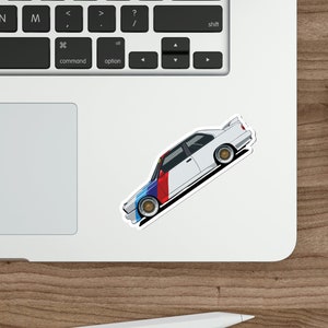 May include: A white BMW M3 race car with blue, red, and white racing stripes. The car is on a white background.