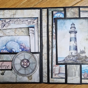 May include: A nautical-themed scrapbook. The open pages display illustrations of a lighthouse, a ship's wheel, and a watercolor painting of a sea creature. The word "Seashore" is printed on a label.