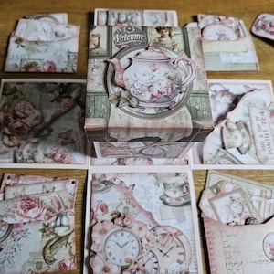 May include: A selection of vintage-style paper ephemera, including cards, envelopes, and a decorative box. The box features a pink teapot design with floral accents and the word "Welcome". The items have a soft, muted colour palette with floral and clock motifs.