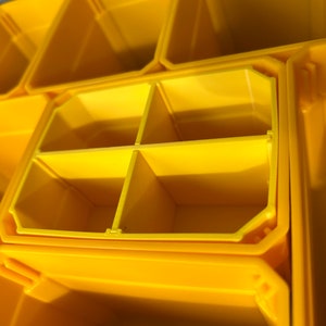 以下が含まれることがあります： 黄色いプラスチック製の収納容器のクローズアップ。容器は4つの小さなコンパートメントに分割されており、グリッド状のパターンになっています。