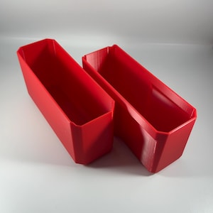 May include: Two red plastic storage containers with a rectangular shape. The containers are empty and have a smooth surface.