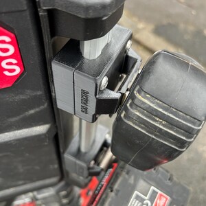 May include: Close-up of a black plastic tool attachment with the text "SLIDE TO RELEASE" printed on it. The attachment is attached to a silver metal pole.