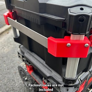 May include: A black and red toolbox with a silver handle and red plastic catches. The toolbox has a wheel on the bottom and the text "Packout cases are not included" is printed on the bottom of the image.