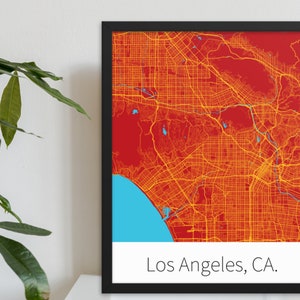 May include: A framed map of Los Angeles, California. The map is in a black frame and features a red background with yellow lines representing streets. The ocean is shown in blue at the bottom of the map. The text "Los Angeles, CA." is printed in black at the bottom of the map.